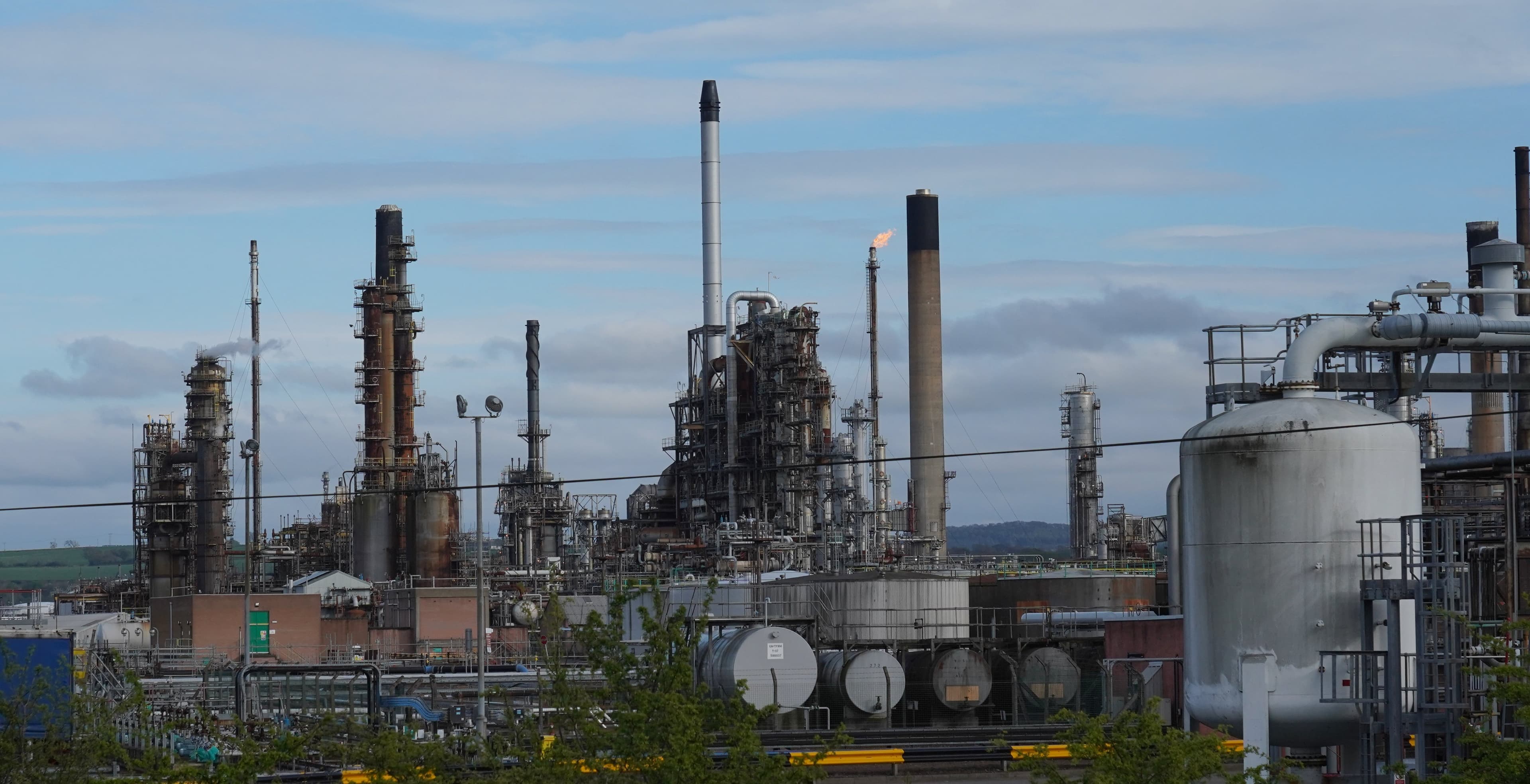 INEOS Grangemouth oil refinery, Scotland, showing distillation towers, storage tanks and a flare stack against a daytime sky.